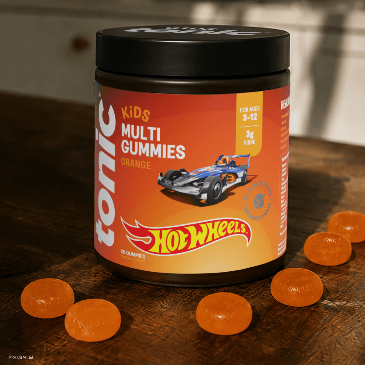 A jar of Tonic Kids Multi Gummies Orange with a Hot Wheels themed label, displayed on a rustic wooden table with several orange gummies scattered around it.