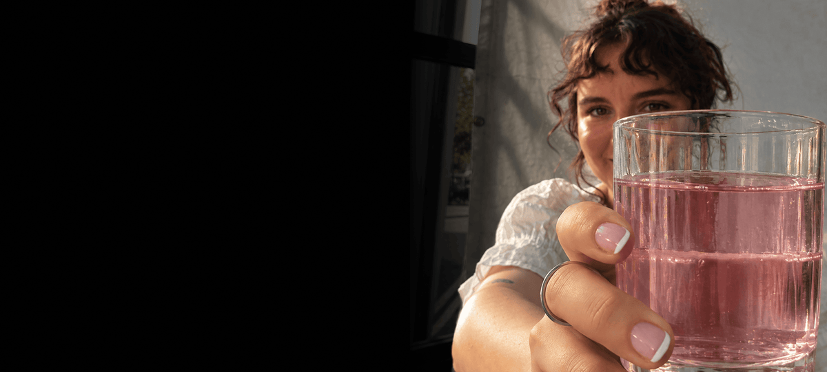 A close-up lifestyle shot of a woman drinking Tonic Creatine + Brain, with strong natural shadows across their face.