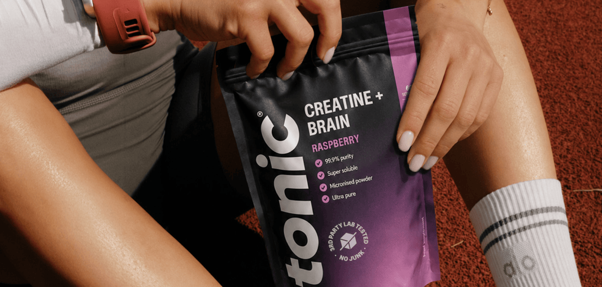 A person holding a pouch of Tonic Creatine + Brain powder in Raspberry flavor. The pouch is black and purple with white text.