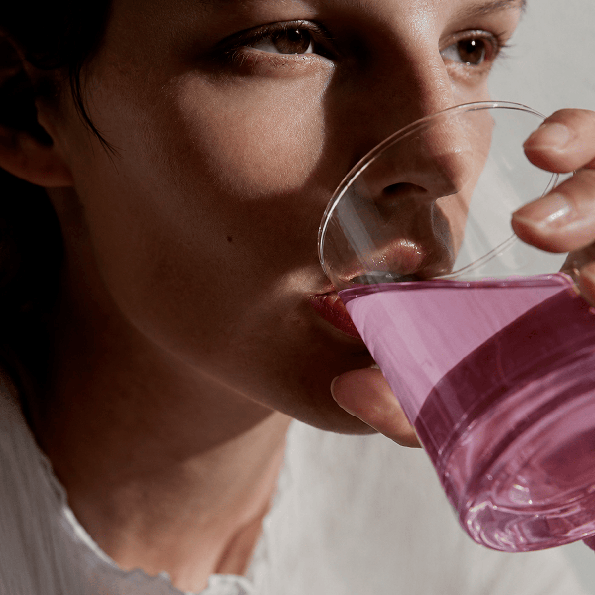 A close-up lifestyle shot of a woman drinking Tonic Creatine + Brain, set against a neutral, softly lit background.