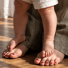 Close-up of a child's bare feet and legs standing on a wooden floor on the parents bare feet.