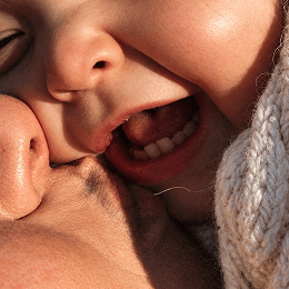 Extreme close-up of a parents face kissing or resting their cheek on their child's cheek, with warm sunlight. 
